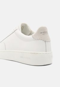 Witte leren sneakers met een gestructureerde beige suède hieltab. Beschikt over een dikke witte zool en gestikte details langs de zijkanten.