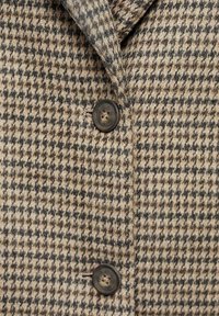 Uldblazer med et hundetandmønster i beige og brun, med en notch-krave og mørk knapdetalje. Tekstureret stoffinish.