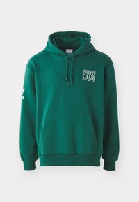 Green hoodie made of soft fabric, featuring a kangaroo pocket, drawstring hood, and white text branding on the chest and sleeve.