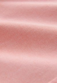 Zbliżenie na miękki różowy materiał o delikatnej, tkanej teksturze i subtelnych fałdach tworzących łagodne cienie.