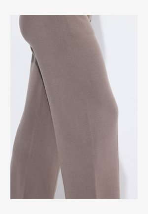 Beige stretch-housut, joissa on sileä rakenne, kapeneva muotoilu ja siistit saumarakenteet. Istuva siluetti korostaa jalkoja.
