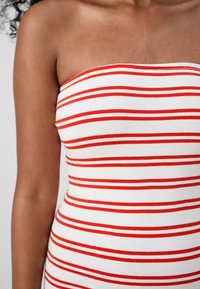 Φόρεμα χωρίς τιράντες με ριγέ σχέδιο σε κόκκινες οριζόντιες ρίγες σε λευκό φόντο, αναδεικνύοντας την ομαλή υφή και την εφαρμοστή σχεδίαση.