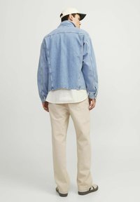 Chaqueta de denim azul claro con un corte relajado, que presenta un cuello alto y una yugo en la parte posterior. Combinada con pantalones beige y una camisa blanca debajo.