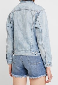 Světle modrá denimová bunda s fitted designem, viditelnými švy a detailními knoflíky, spárovaná s roztrhanými denimovými šortkami.