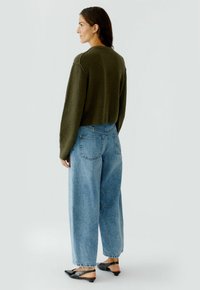 Olivgrüner verkürzter Pullover, hellblaue lockere Jeans, schwarze spitze Ballerinas. Texturstoff, entspannte Passform, sichtbare Taschen und Bündchen.