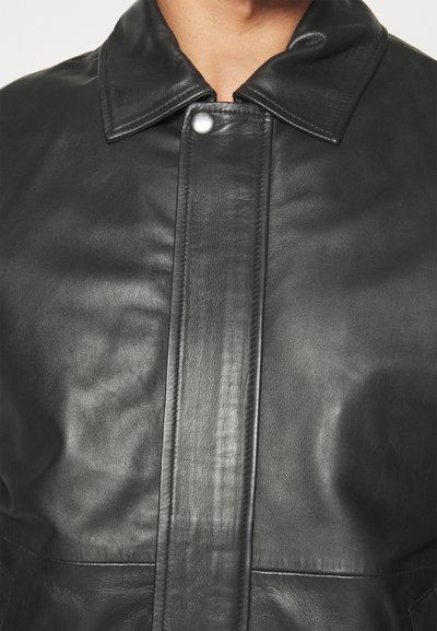 Svart läderjacka med krage, knappstängning och slät yta. Har framträdande sömmar och fickor.