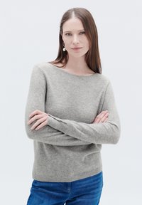 Maglione in cashmere grigio chiaro con scollo rotondo, fondo a coste e maniche lunghe indossato da una persona con jeans blu.