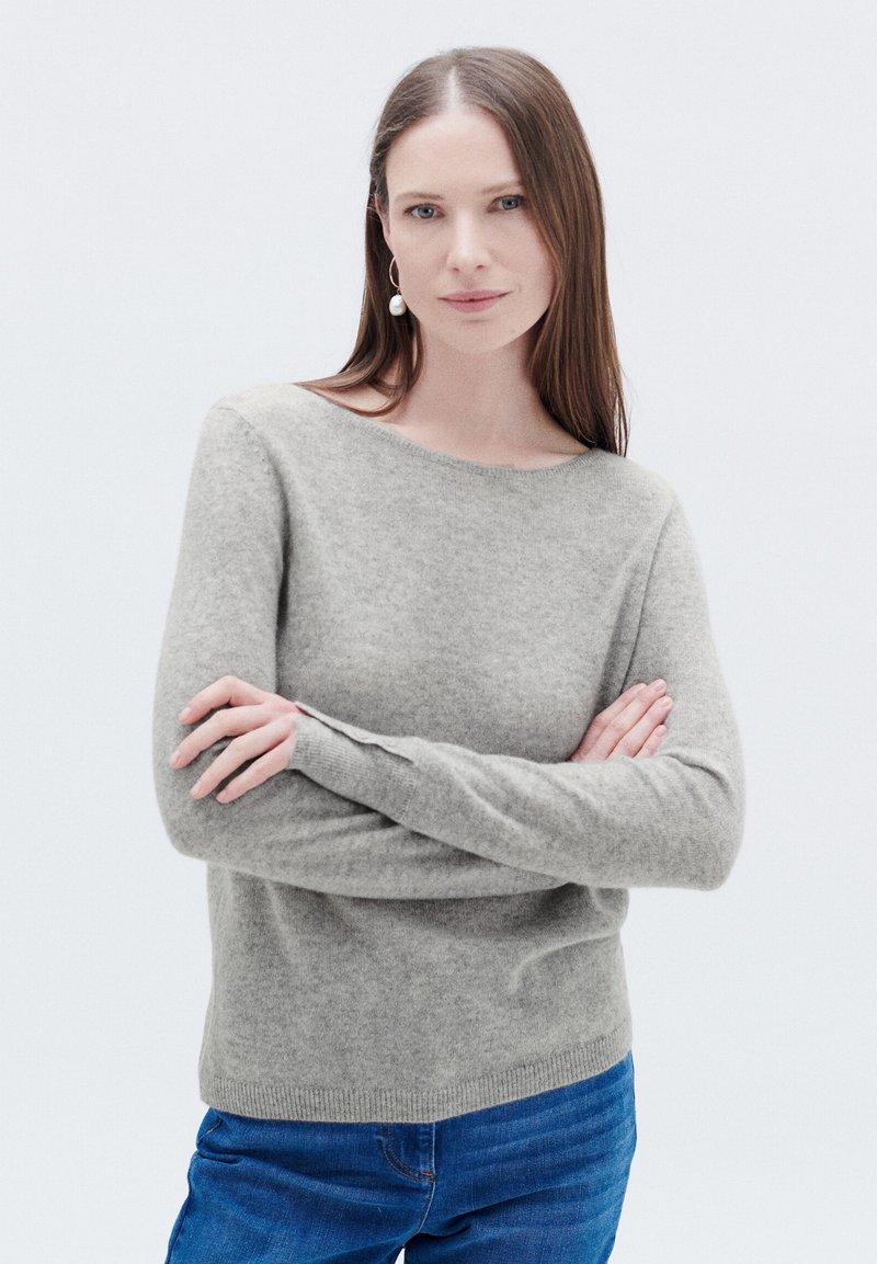 Maglione in cashmere grigio chiaro con scollo rotondo, fondo a coste e maniche lunghe indossato da una persona con jeans blu.