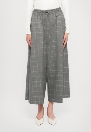 Pantalon gris à jambe large et raccourci avec un motif à carreaux subtil, taille élastique avec cordon, porté avec des chaussures blanches pointues et un haut blanc.