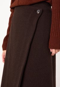 Gonna avvolgente di lana marrone con un design diagonale, una texture sottile e una chiusura con bottone in vita, abbinata a un maglione rigato color maroon.