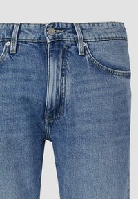 Jasnoniebieskie dżinsy z denimu o klasycznym kroju z pięcioma kieszeniami, zapinane na metalowy guzik, z lekko zwężanymi nogawkami i miękką teksturą.