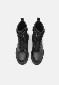 Par af sorte læder snørebånd ankelstøvler med sidelommer, tykke såler og trækflapper, set ovenfra på en hvid baggrund.