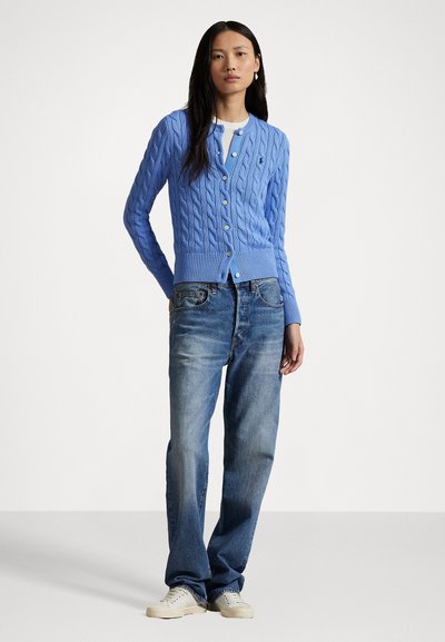 Cardigan en tricot câblé bleu clair avec un décolleté en V, cinq boutons et des poignets côtelés, associé à un jean droit délavé bleu et des baskets claires.