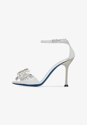 White high-heeled sandal with a clear band and crystal embellishments. Features an ankle strap and a contrasting blue sole. Elegant and sleek design.