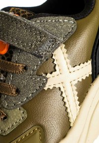 Sneaker in pelle verde oliva con toppe di suede testurizzato, strap in velcro, lacci marroni e dettagli di cucitura a zigzag. Presenta elementi in rete.