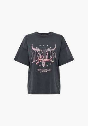 T-shirt oversize gris foncé avec texte « Desert Rebel » rose et blanc, étoiles et graphique de crâne de taureau centré sur le devant.