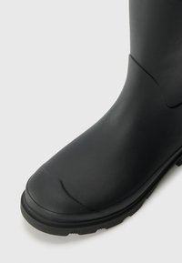 Botte en caoutchouc noire avec un bout rond, finition texturée, et une semelle robuste dotée de motifs de semelle pour une meilleure adhérence. Design lisse sans embellissements.