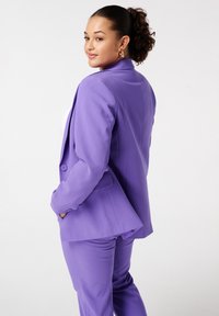 Paarse op maat gemaakte broekpak met een single-button blazer en slim fit broek. Soepele stof, gestructureerd ontwerp en een uitgesneden revers voegen detail toe.