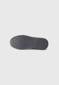 Black rubber shoe sole with a textured pattern of circular shapes and grooves. Smooth edges and a slight curve at the heel.