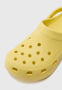 Yellow clogs featuring a textured upper with multiple ventilation holes and a molded design, curved shape, and a raised heel for comfort.