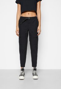 Svarta cargobyxor med elastisk midja, bälte och sidofickor, med en avsmalnande bendesign och manchetter i nederkant, i kombination med svarta sneakers.