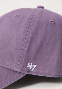Purple cotton cap with curving brim, stitched texture, and white embroidered "47" logo on the side. Features a fabric button on top.