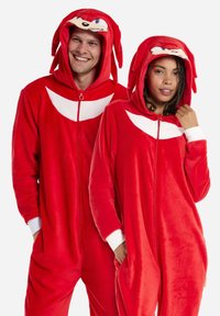 Red fleece onesies with hood featuring a cartoon character's face. White accents on chest and cuffs. Zipper front and side pockets.