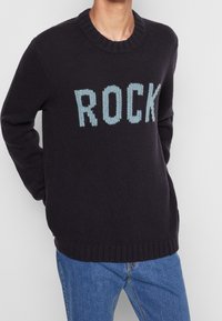 Dunkelblauem gestricktem Pullover mit dem Wort "ROCK" in Hellblau. Runder Ausschnitt, gerippte Bündchen und Saum, lässige Passform. Angepasste Ärmel.