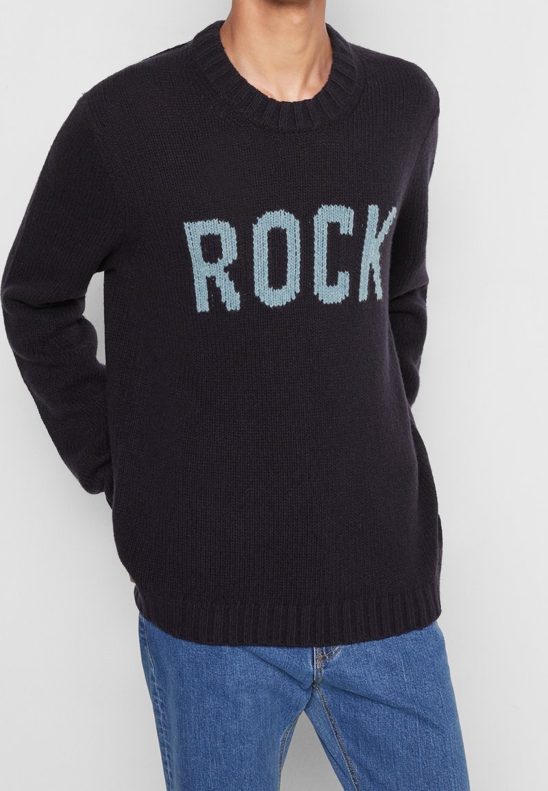 Dunkelblauem gestricktem Pullover mit dem Wort "ROCK" in Hellblau. Runder Ausschnitt, gerippte Bündchen und Saum, lässige Passform. Angepasste Ärmel.