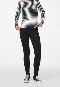 Svarta jeans tillsammans med en långärmad topp i svart och vitt randigt. Toppens yta har en ribbad struktur och en rundad halsringning.