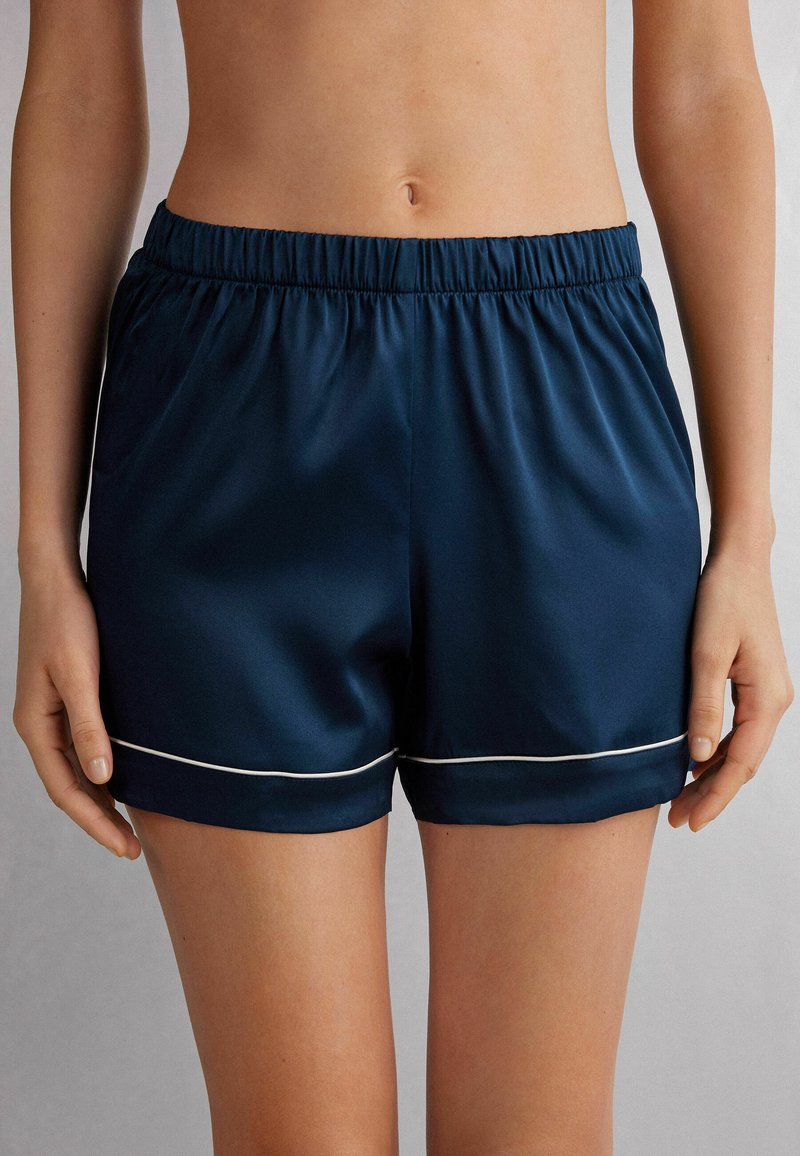 Námořnické modré sportovní šortky z hladkého materiálu, s elastickým pasem a bílým lemováním na spodním okraji. Délka do poloviny stehna.