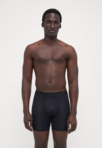 Fekete boxer alsónadrág rugalmas anyagból, puha derékrésszel, amelyen a márkaneve található. Testhez simuló fazon, nincsenek látható minták.