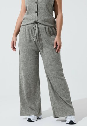 Kobieta ubrana w szare, prążkowane, szerokie spodnie z dzianiny z troczkiem w pasie oraz dopasowaną kamizelkę na guziki, w parze z białymi trampkami.