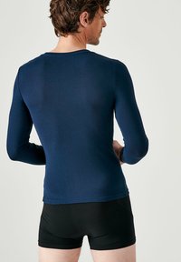 Top lungo navy in materiale elasticizzato con collo rotondo, abbinato a pantaloni corti neri aderenti, visti da dietro.