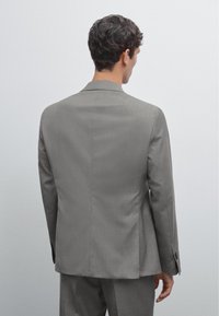 Grauer Anzugjacke aus strukturiertem Stoff, mit einem Rückenschlitz, Knotenrevers und geknöpften Manschetten. Minimale Details und maßgeschneiderte Passform.