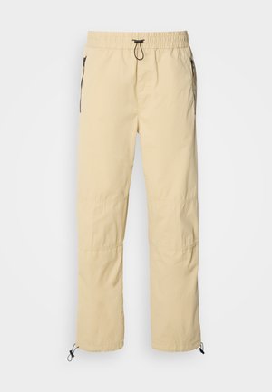 Light yellow lightweight pants with an elastic waist, drawstring, and black zippered pockets, featuring a tapered leg and adjustable hems.