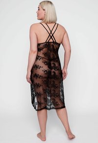 Zwarte kanten nachtjapon met bloemenborduursel, met een ontworpen sheath, doorschijnende textuur en crisscross bandjes op de rug. Lengte tot halverwege het kalf.