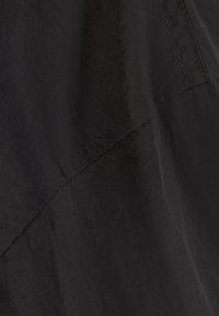 Black fabric with a smooth texture, featuring a stitched seam. The design is minimalist with a focus on clean lines and lack of patterns.