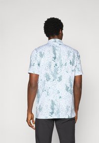 Short-sleeve shirt with a light blue base and green splatter pattern, featuring a collared neck and a relaxed fit. No visible graphics or hardware.