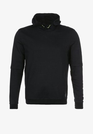 Sweat à capuche noir avec un col haut, associé à des leggings de sport noirs mi-longs avec des rayures sur les côtés, et des baskets noires.