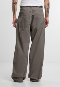 Helle graue Hose mit weitem Bein aus einem weichen Stoff, ausgestattet mit zwei Gesäßtaschen und einem lockeren Schnitt.