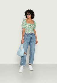 Top cropped com padrão floral e mangas bufantes, combinado com jeans desgastados de tom azul claro. Acessórios incluem uma bolsa azul clara e sapatilhas brancas.