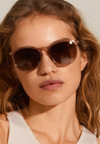Sunglasses with a light pink transparent frame and dark brown lenses; rounded shape with thin temples, suitable for casual wear.