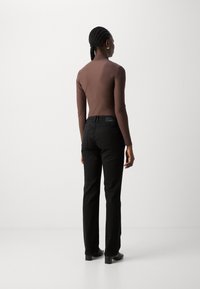 Bruine lange mouwen bodysuit gecombineerd met zwarte rechte jeans. Glad materiaal en een aansluitend ontwerp met minimalistische hardware en subtiele details.