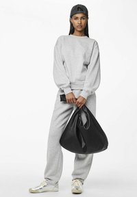 Gray sweatshirt and sweatpants with a relaxed fit, paired with a large black textured bag. Silver shoes feature a smooth finish.