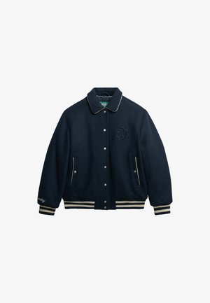 Navy wool blend varsity jacket with a collared neck, silver snap buttons, side pockets, and cream-striped ribbed cuffs and hem. Logo embroidered on chest.
