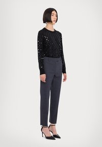 Μαύρος πλεκτός πουλόβερ με λαμπερό σχέδιο από παγιέτες, συνδυασμένο με κομψό γκρι παντελόνι και μαύρες στιλέτο γόβες. Απλός κόσμος για έμφαση.