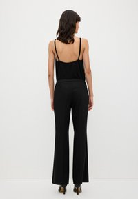 Zwarte tanktop met dunne schouderbandjes, open rugdetail, gecombineerd met zwarte flared broek en hoge hakken, wat een slanke silhouette benadrukt.