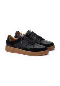 Zapatillas negras con una combinación de cuero liso y ante, con detalles perforados, cordones negros y una suela de goma marrón.