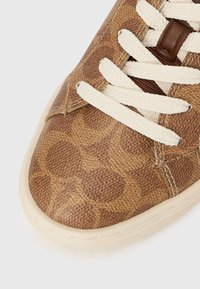 Baskets marron avec un motif texturé, des lacets crème et une semelle en caoutchouc claire. Dotées d'une tige lisse ressemblant à du cuir et de détails de couture.